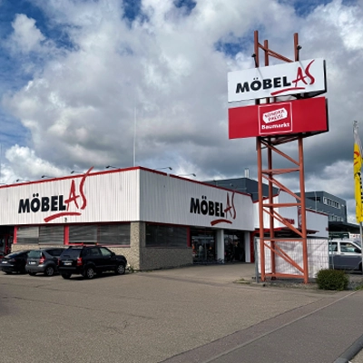 Möbelgeschäft in Ellwangen mit einem großen Parkplatz und einem Werbeschild, das "Tapeten, Gardinen, Bodenbeläge" anzeigt.
